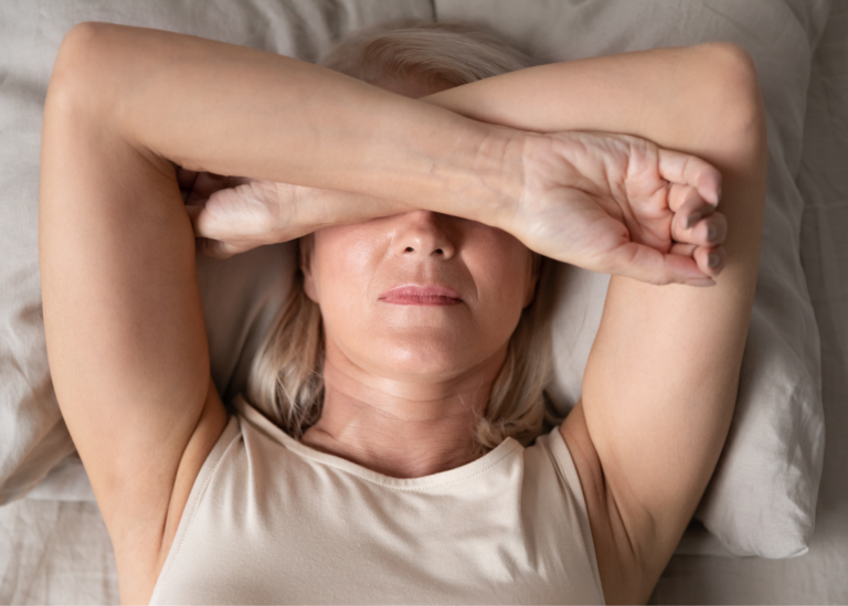 woman lying in bed arms crossed over face displaying stress.