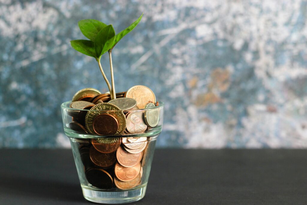A young green plant sprouting from a glass jar of coins, symbolizing financial growth and long-term investment strategies